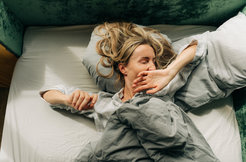 Eine Frau streckt sich nach dem Aufwachen und gähnt im Bett liegend.